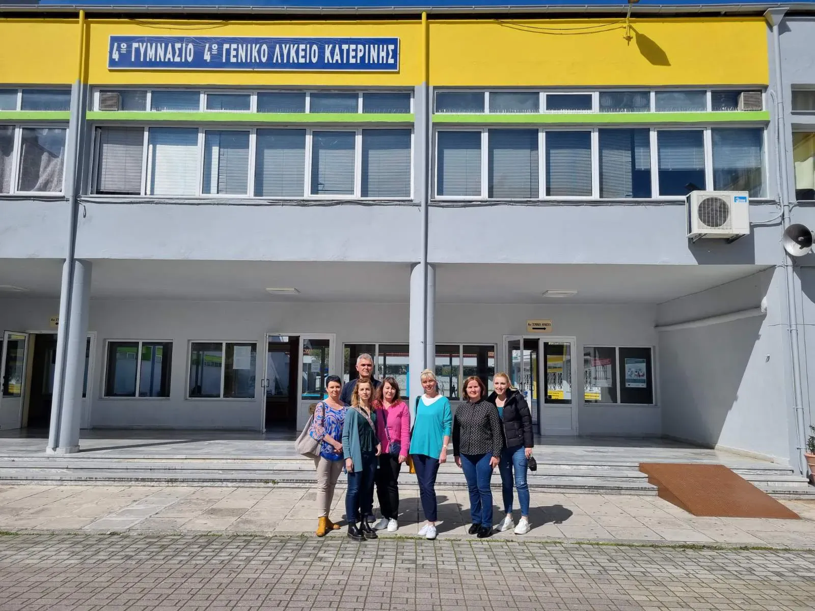 ludzie pozujący przed budynkiem z żółtym i zielonym znakiem